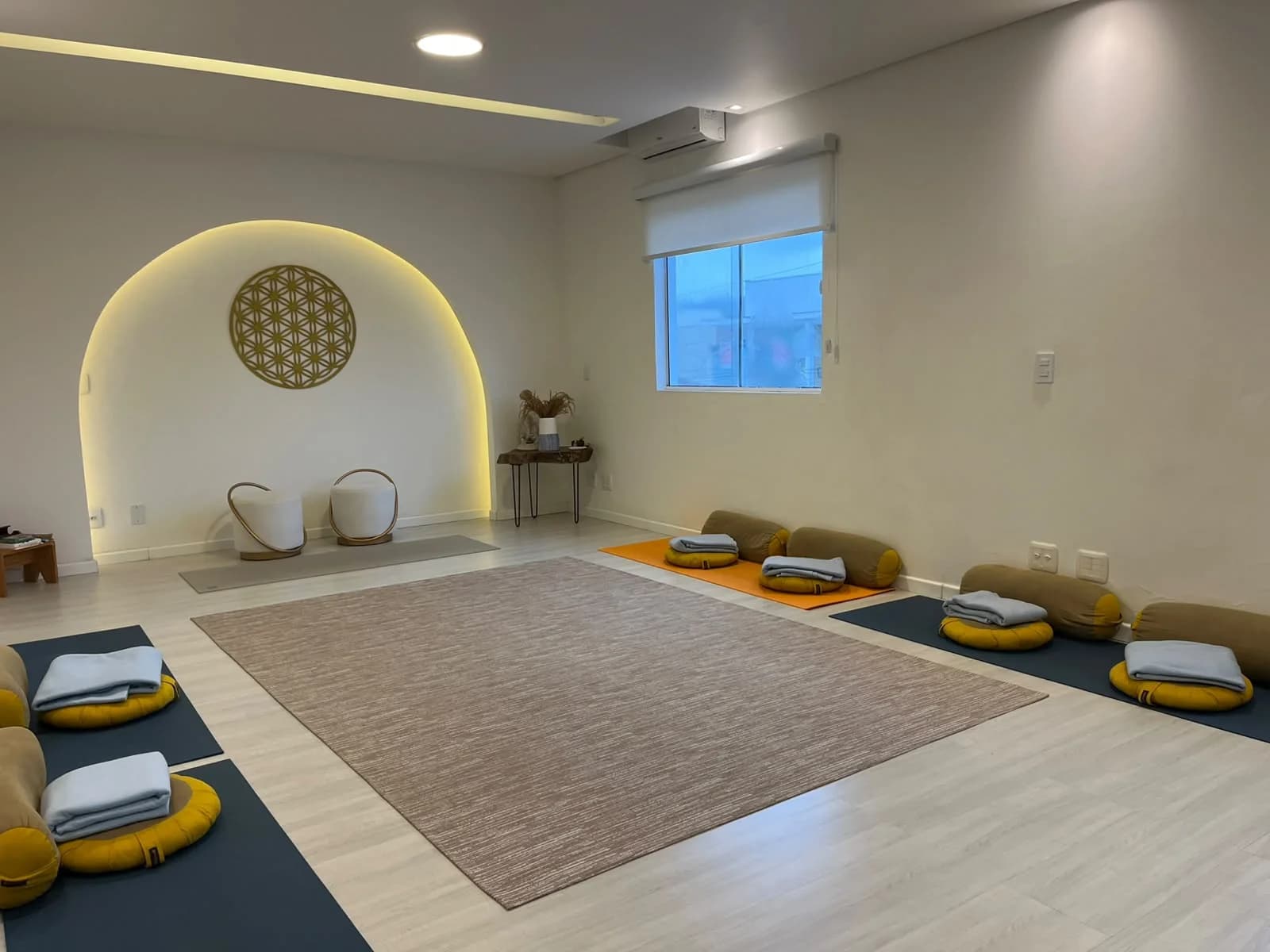 Sala dos encontros vista de frente: tapete ao centro, almofadas e mantas sobre colchonetes nas laterais e o nicho em arco iluminado ao fundo